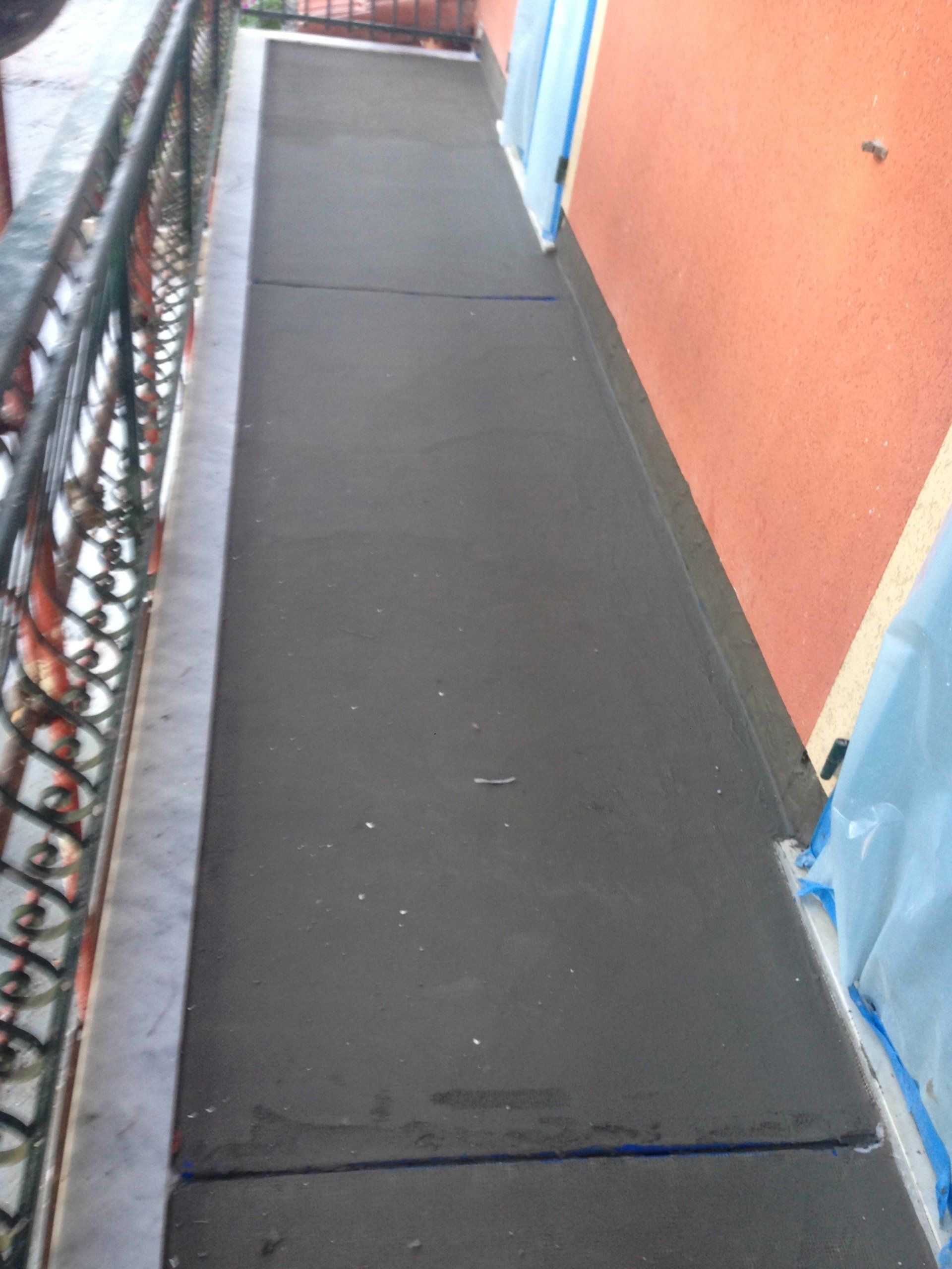 Stretto balcone esterno con pavimento grigio scuro e parete arancione.