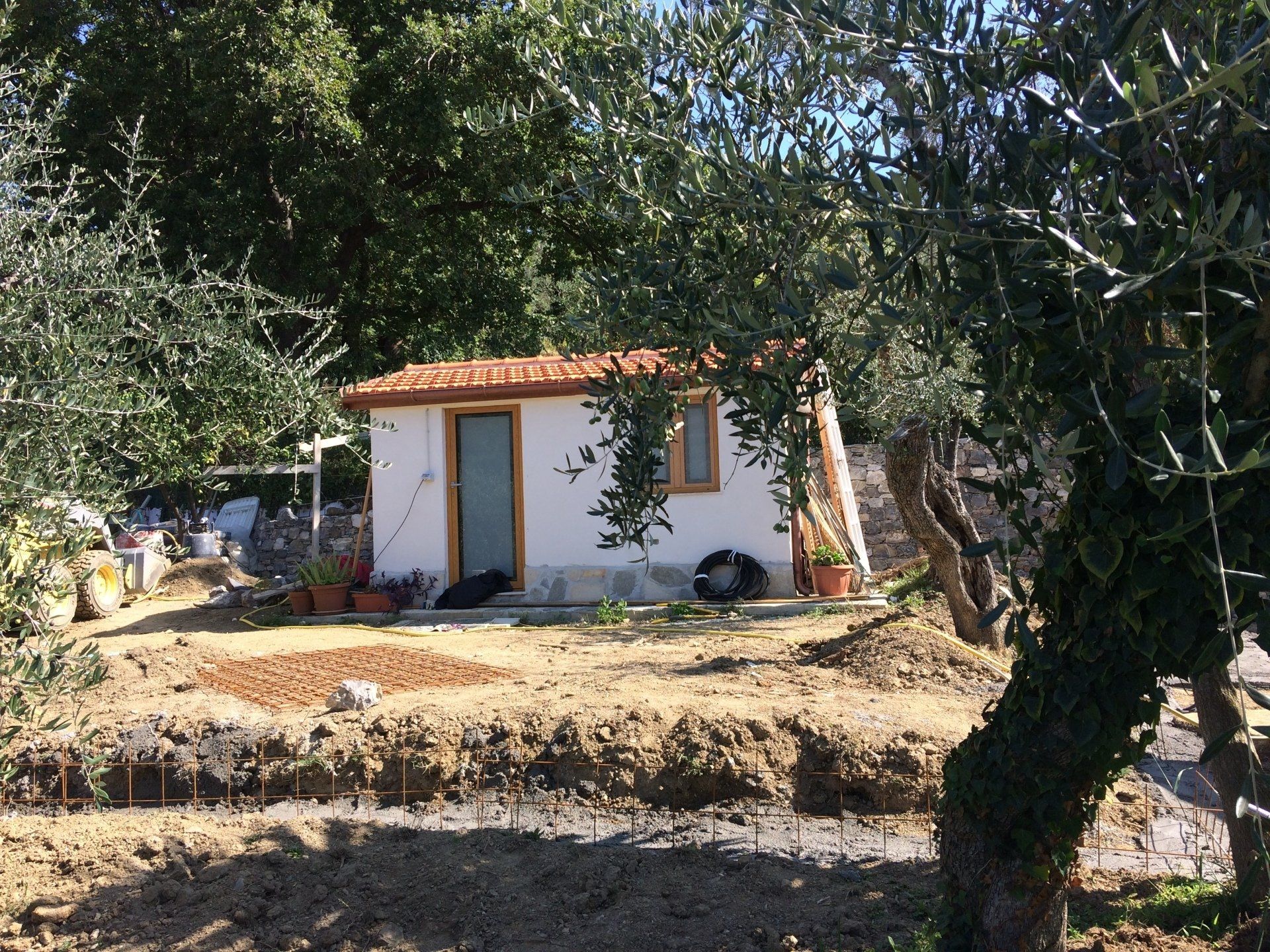 Piccola casa bianca con tetto di tegole arancioni in un cortile, incorniciata da alberi.