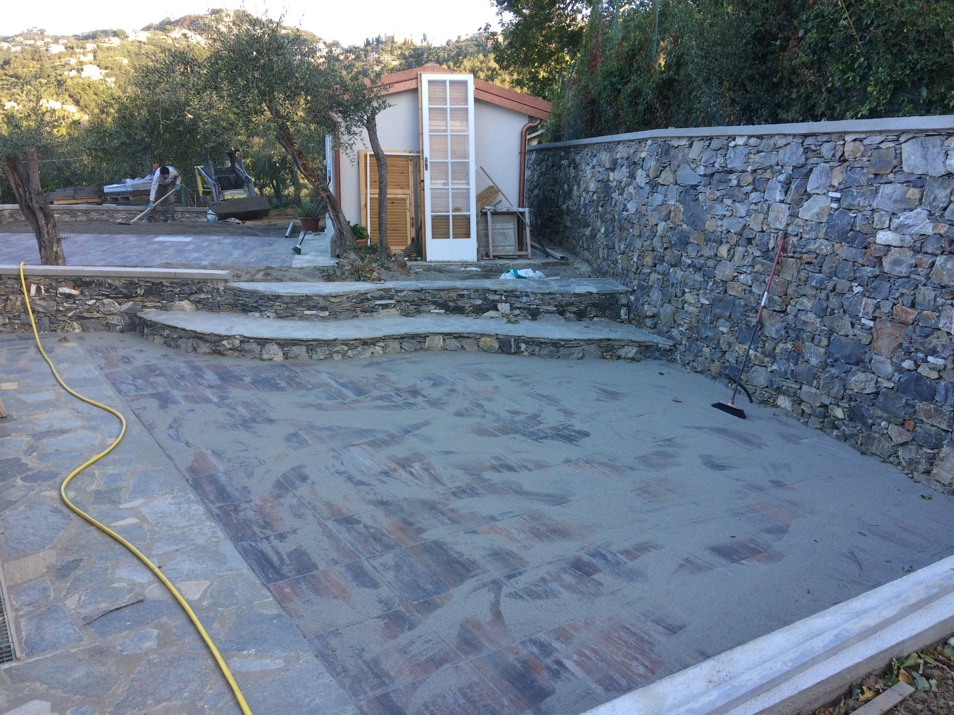 Una piscina in costruzione con muri in pietra e gradini; sullo sfondo un piccolo capanno.