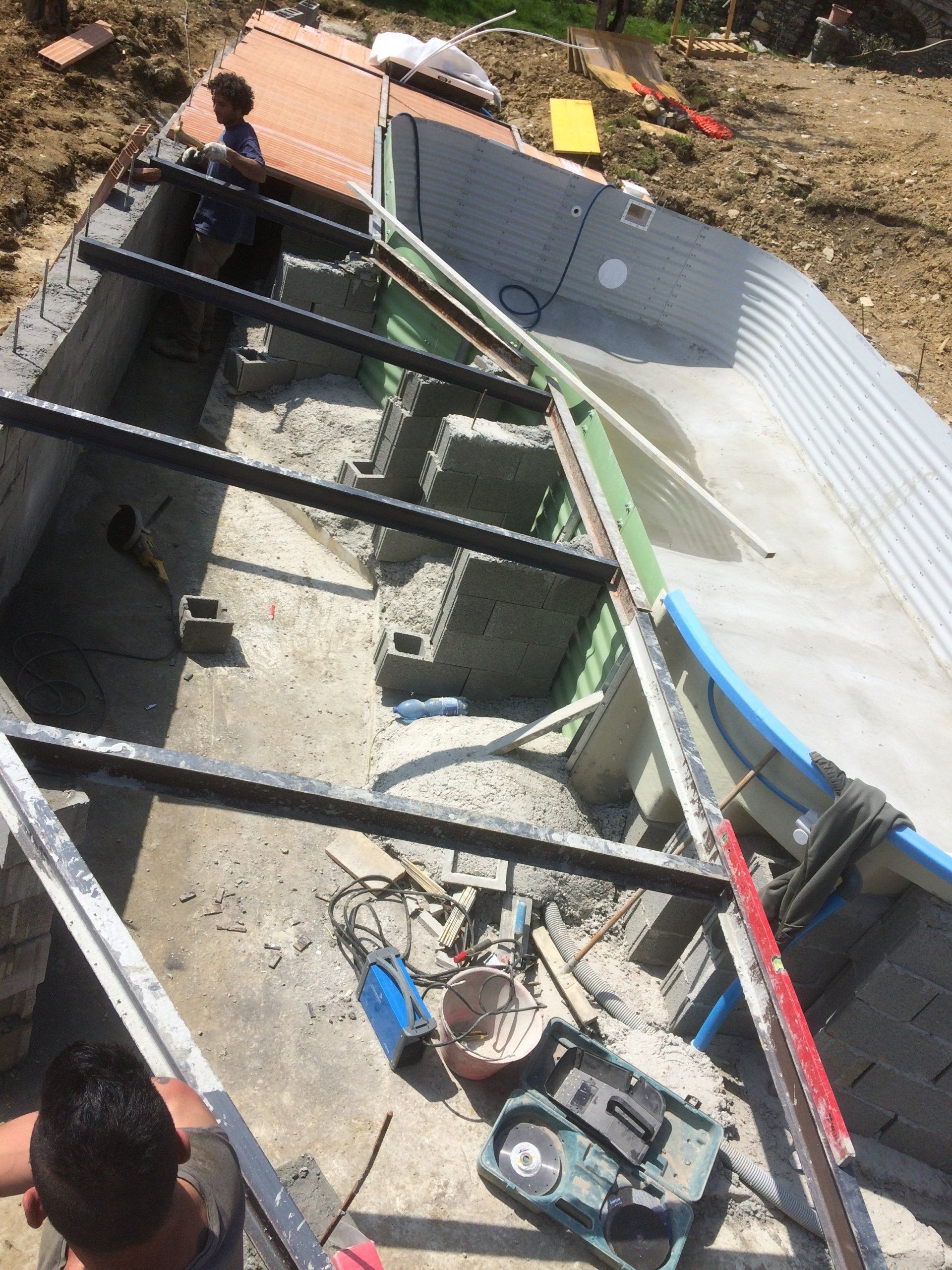 Costruzione di una piscina: operai saldano travi metalliche all'interno di una struttura in cemento e lamiera ondulata.