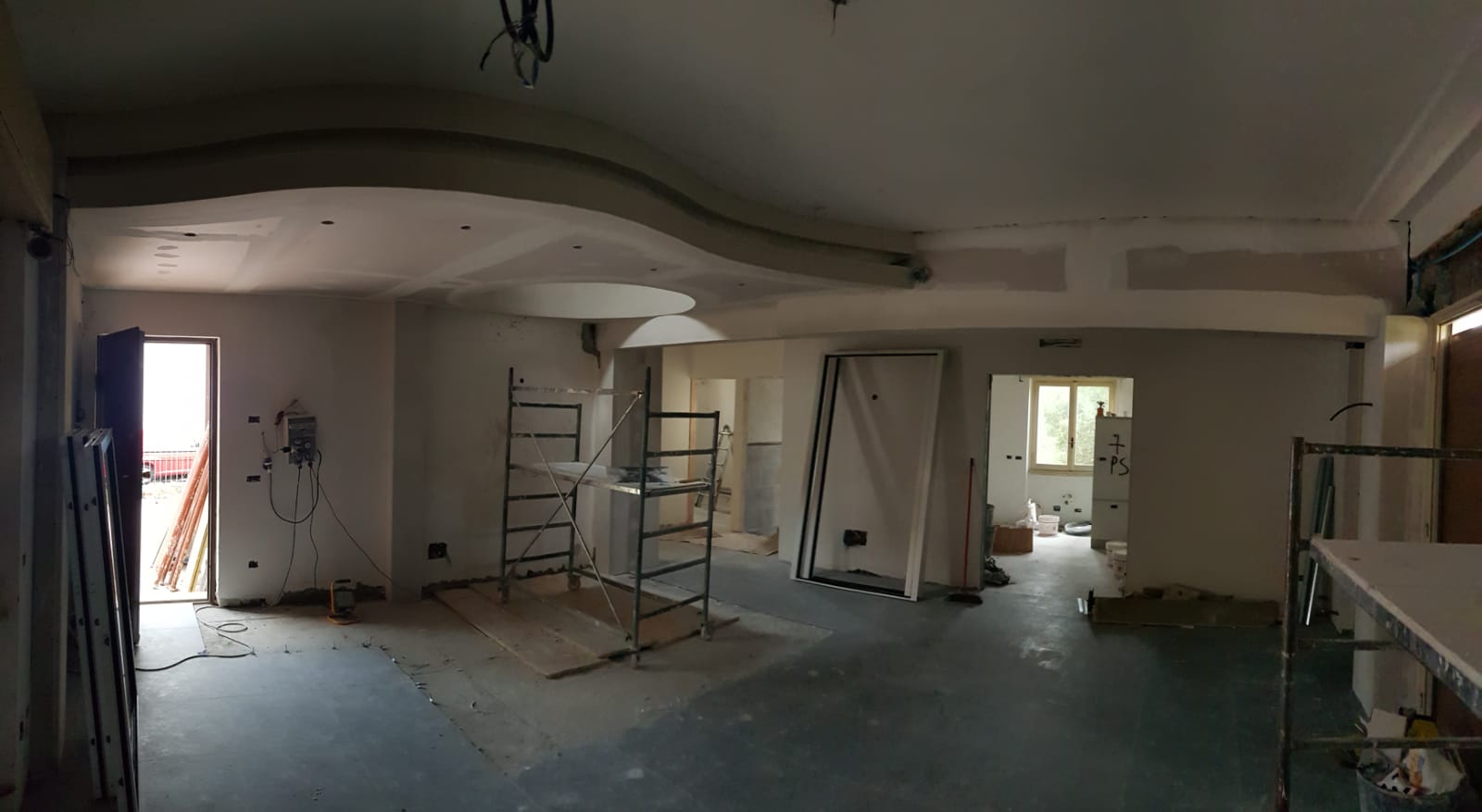 Interno di una stanza in costruzione, con cavi elettrici, impalcature e pareti non finite a vista.