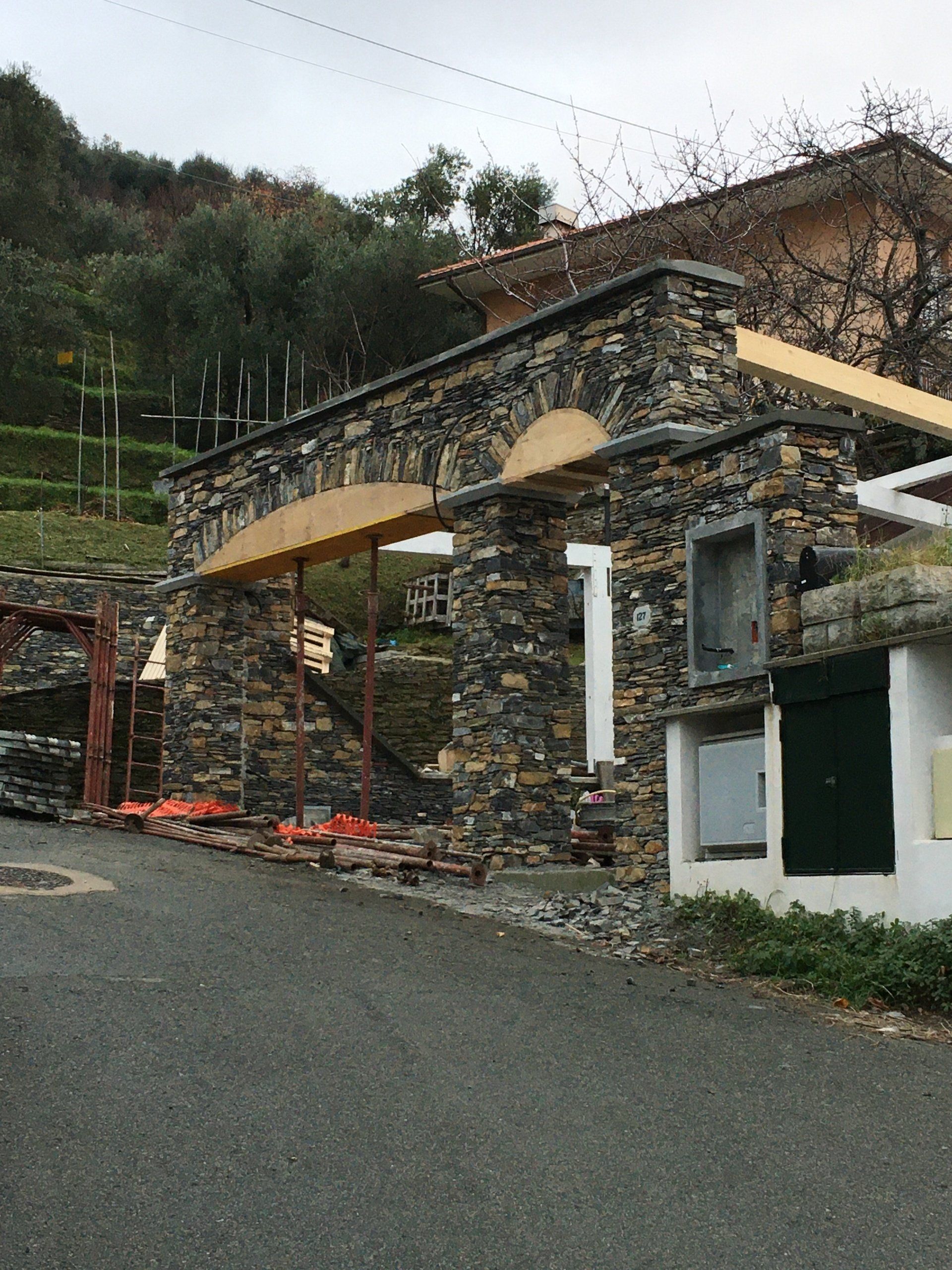 Arco in pietra in costruzione su una strada. Un'impalcatura sostiene gli elementi incompiuti, con una collina sullo sfondo.