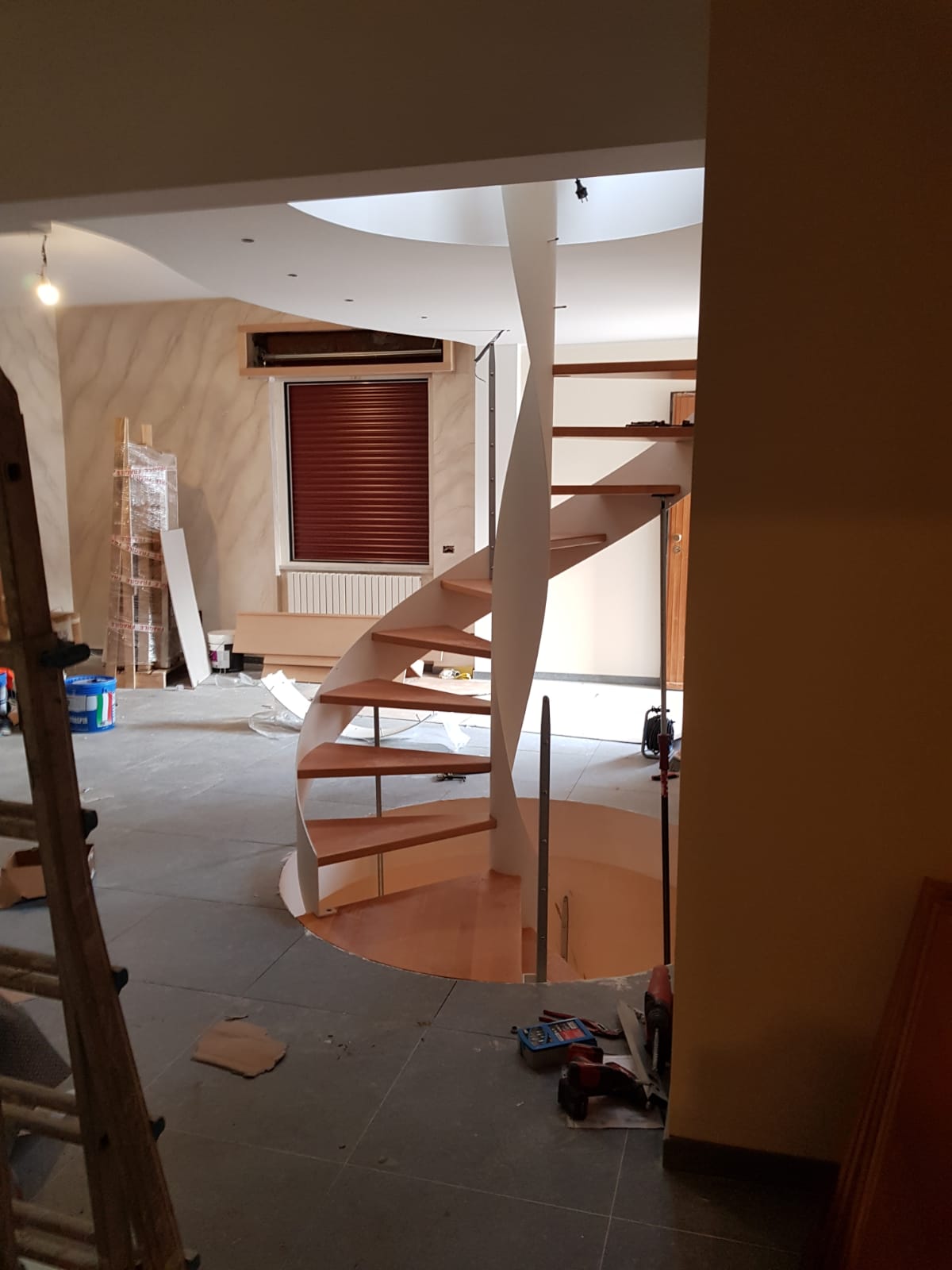 Scala a chiocciola con gradini in legno e supporto bianco in una stanza in costruzione.