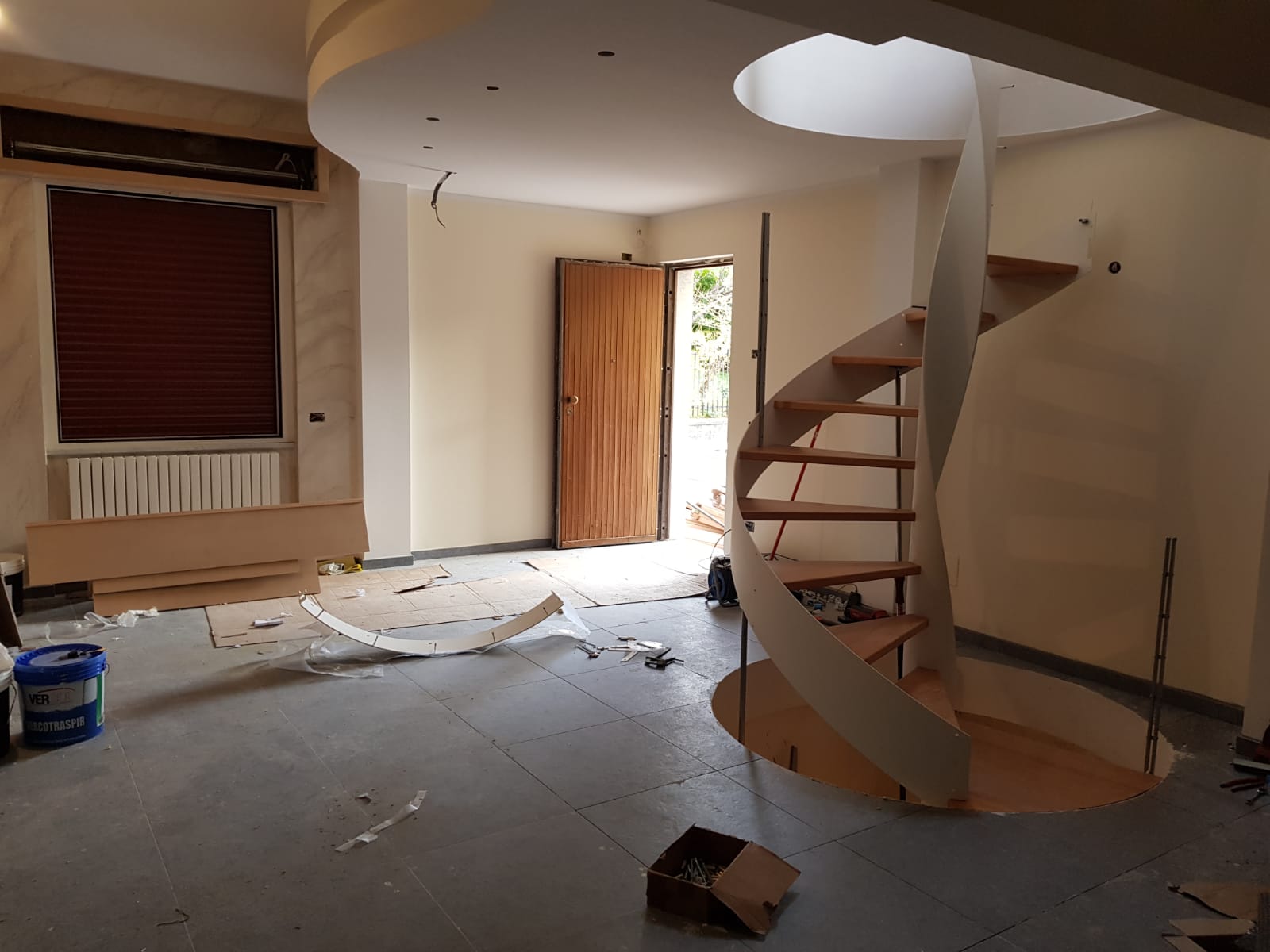 Interno con scala a chiocciola, porta e finestra con persiane in costruzione.