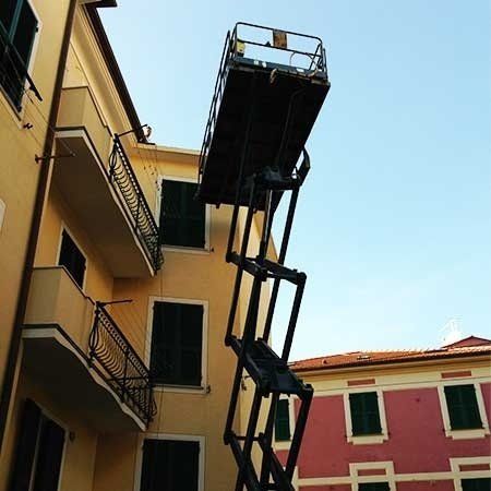 Piattaforma elevatrice estesa per accedere al tetto di un edificio; edificio giallo sulla sinistra, edificio rosa sulla destra, cielo azzurro.