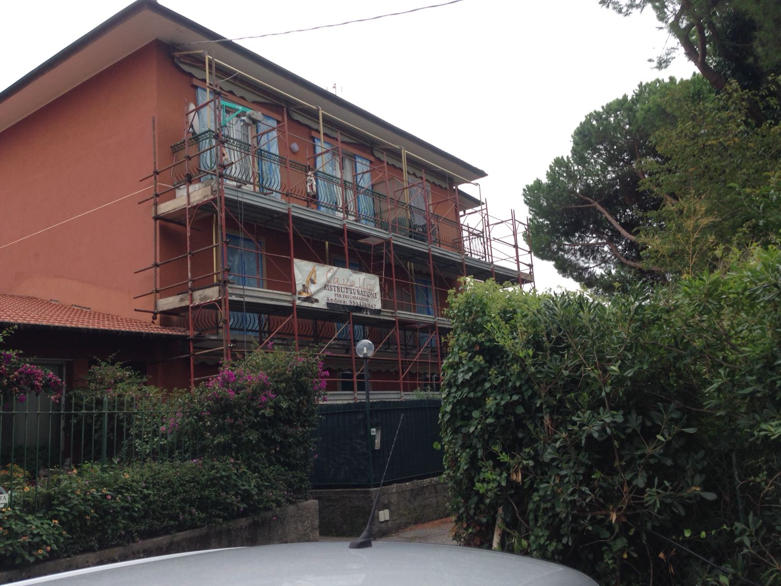 Edificio rosso con impalcature; cespugli e alberi di fronte.