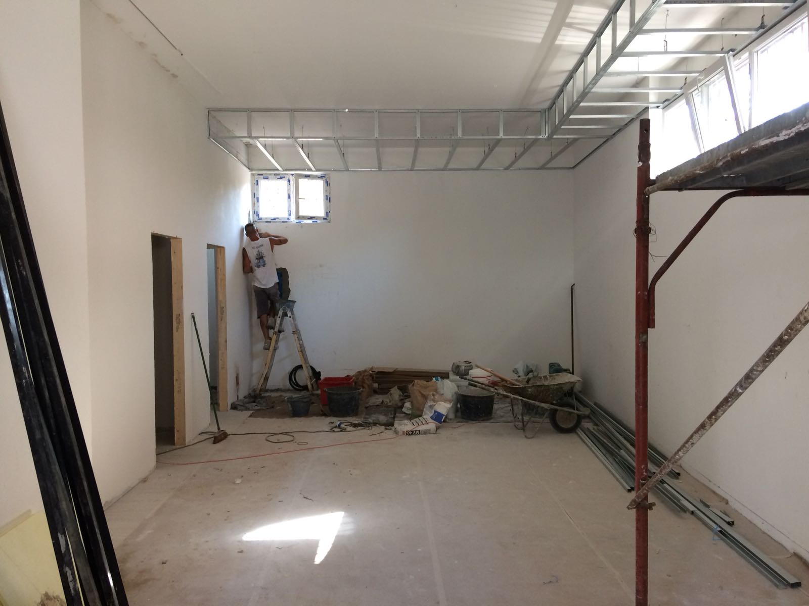 Stanza in costruzione, operaio su una scala vicino alla finestra, struttura metallica sul soffitto.