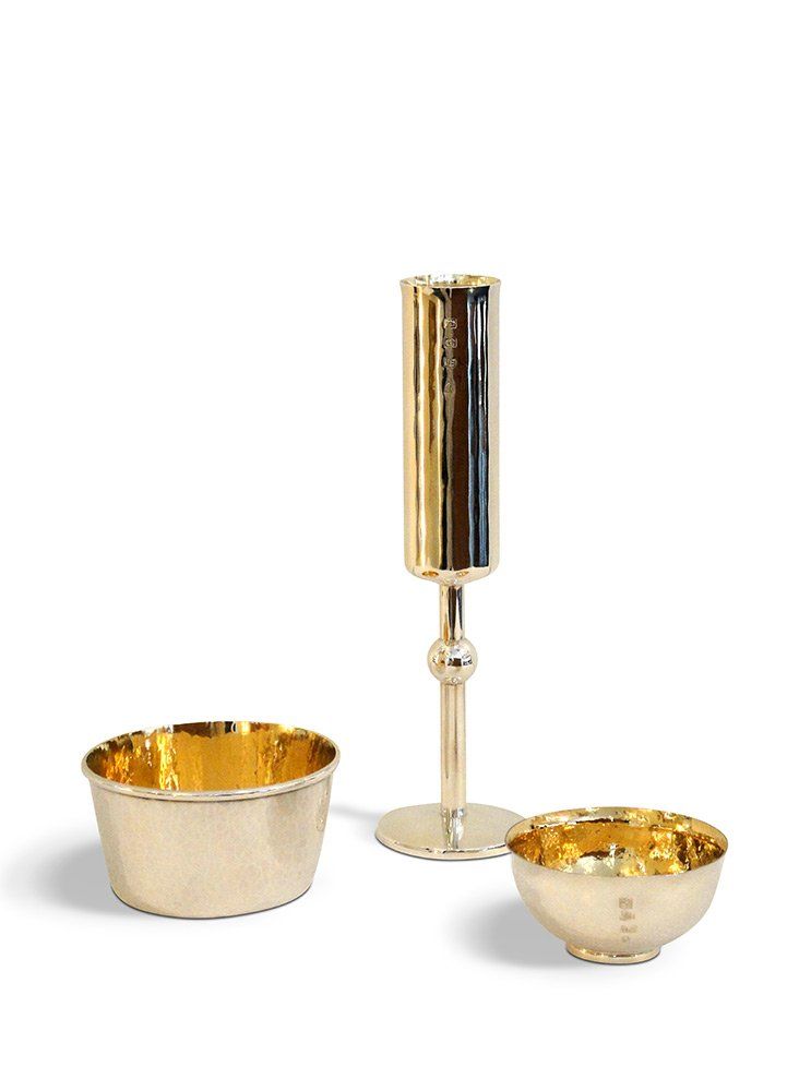 Ein goldenes Weinglas und zwei goldene Schalen auf weißem Hintergrund.