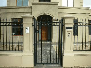 Black iron gate and fence in front of a light-colored building with a wooden door, number 