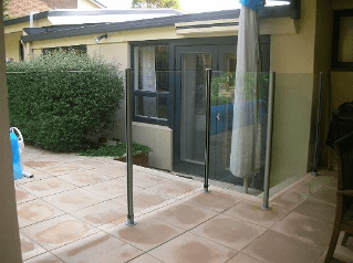 Glass and metal barrier on patio, with a door and shrubbery in the background.