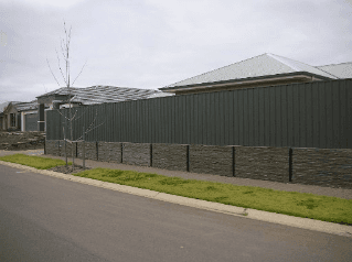 A gray fence with stone base along a street in front of a house on an overcast day.