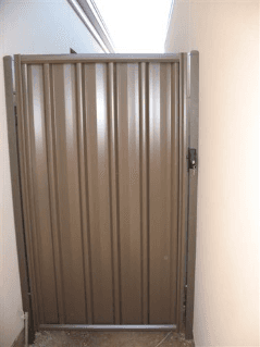 Brown metal gate set in a narrow space with off-white walls.