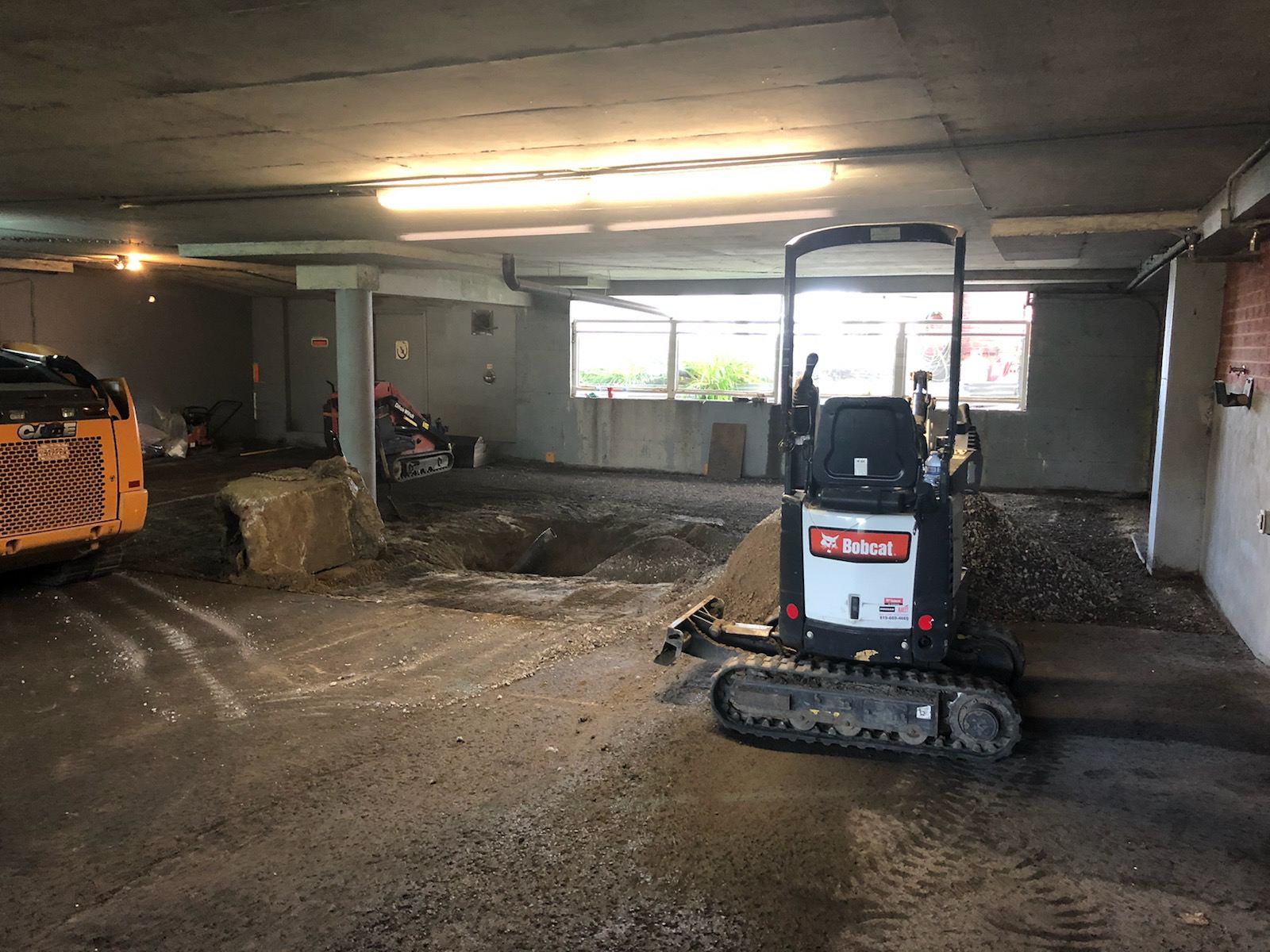 Un chantier de construction intérieur avec une excavatrice Bobcat et des débris.