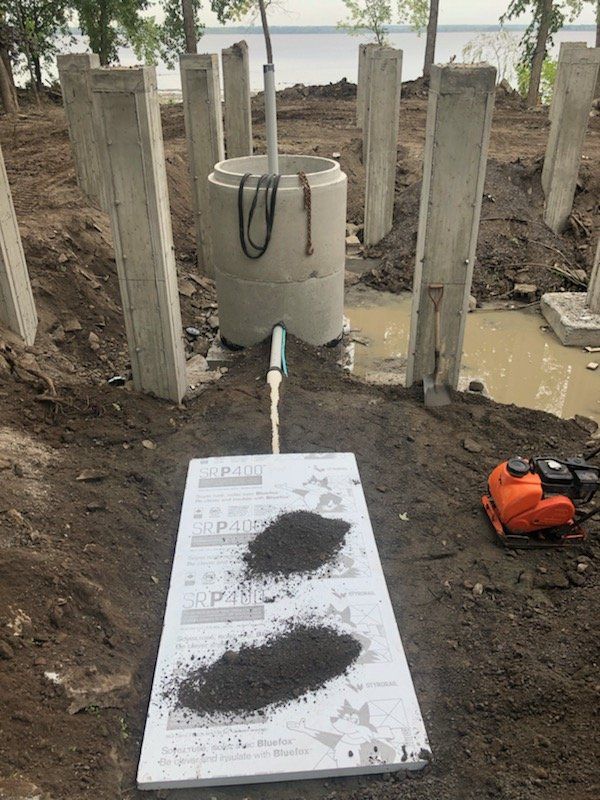Chantier : Piliers en béton, puits et équipements enfouis dans la terre, près de l'eau.