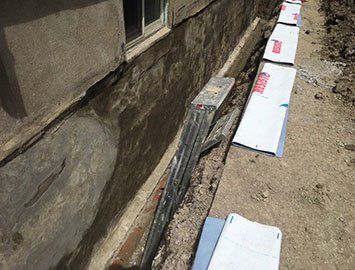 Réparation des fondations : tranchée creusée le long d'un bâtiment en béton, mettant à nu les fondations.