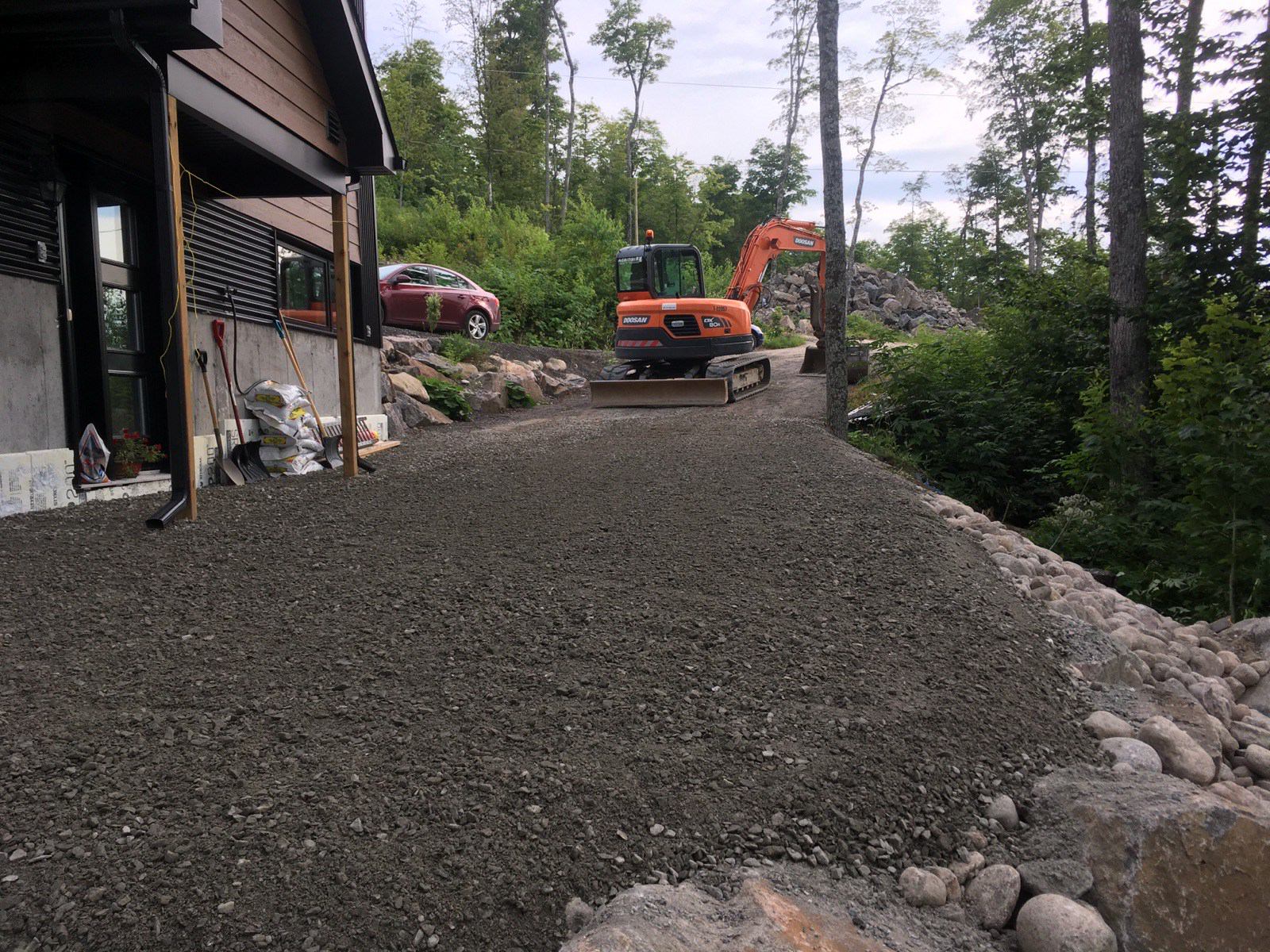 Chantier de construction avec allée en gravier, mini-pelle et maison partiellement construite.