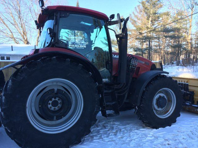 Tracteur rouge Case IH stationné dans une zone enneigée, avec une lame à neige à l'avant.