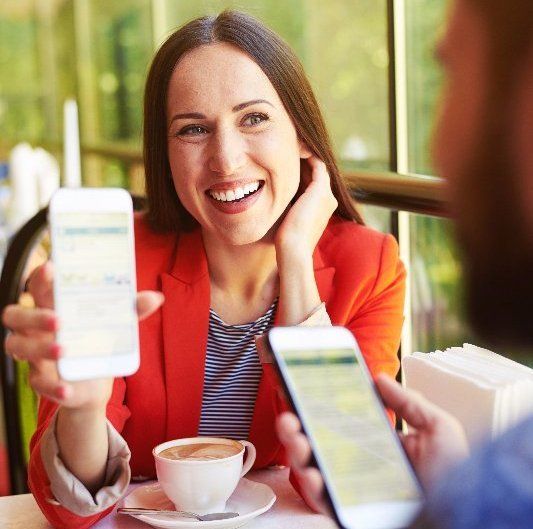A woman is sitting at a table with a cup of coffee and holding two cell phones.