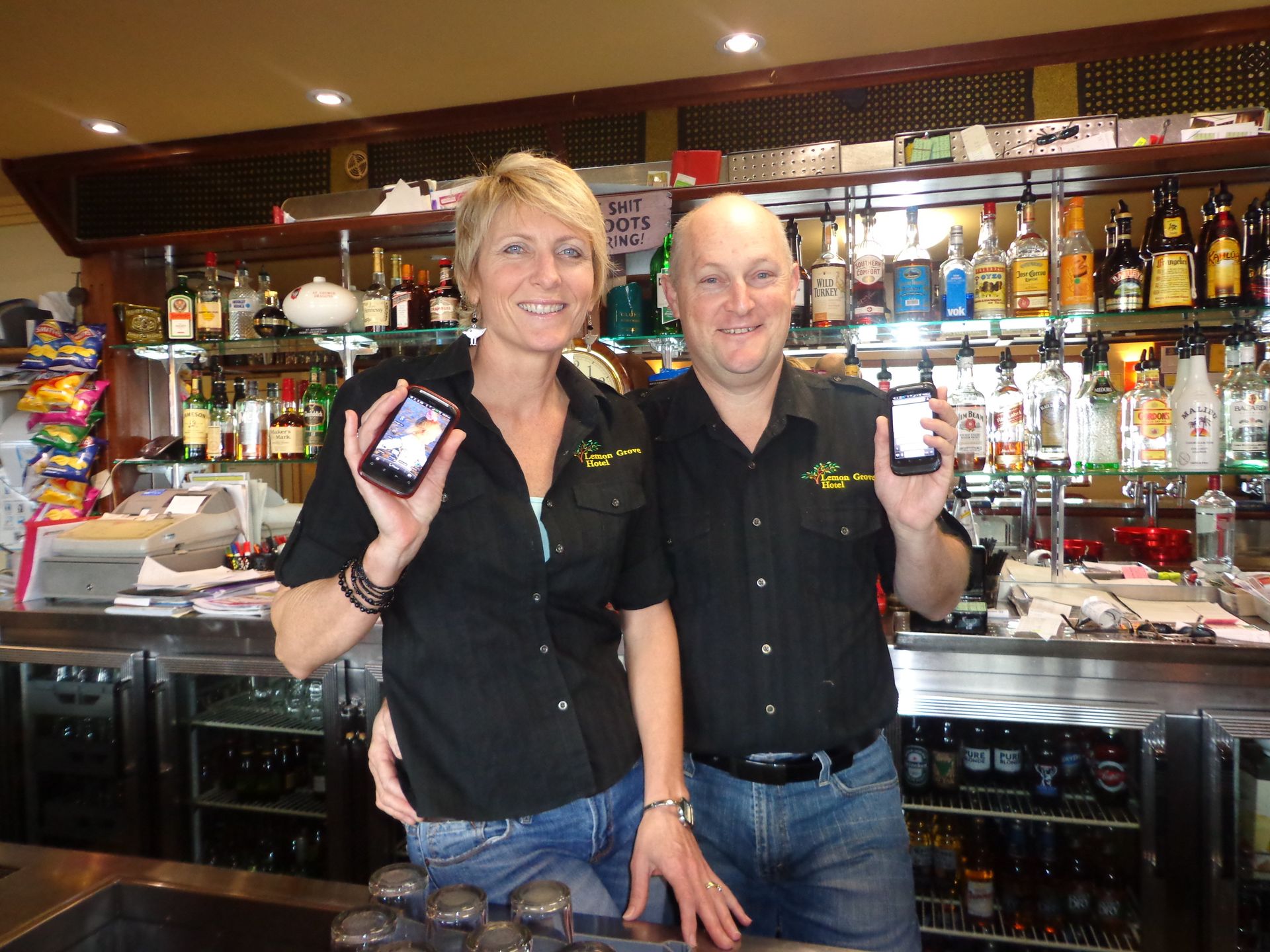 A man and a woman standing in front of a bar holding cell phones