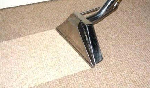 Carpet cleaner nozzle vacuuming beige carpet, leaving a cleaned strip