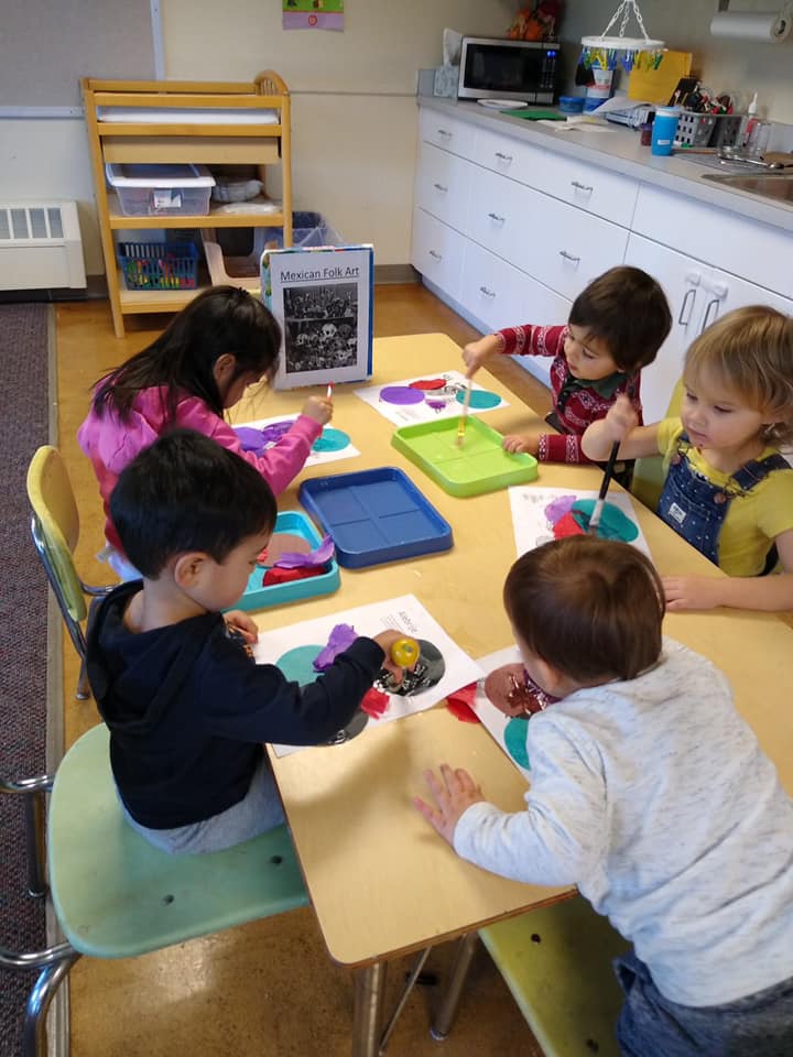 A group of children are sitting at a table in a classroom.