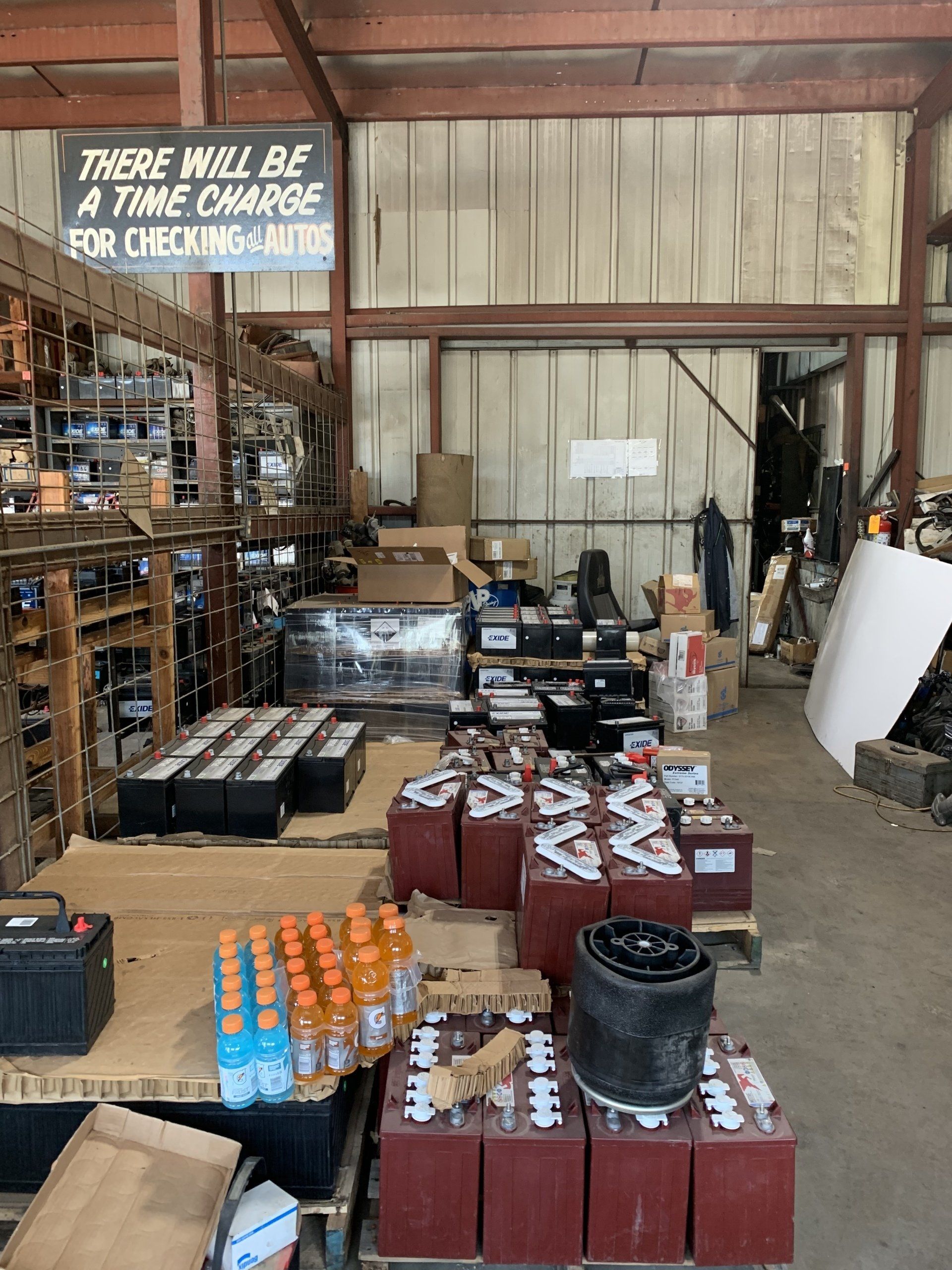 A warehouse interior filled with rows of large industrial batteries, with a sign indicating a time charge for checks.