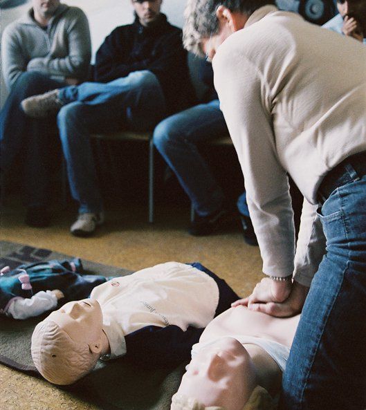 Übungseinheit, bei der eine Person an einer Reanimationspuppe die Herzdruckmassage übt, während andere zusehen.