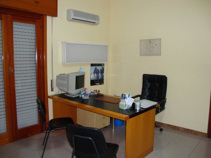 Ufficio con scrivania, computer, sedie nere e una finestra.