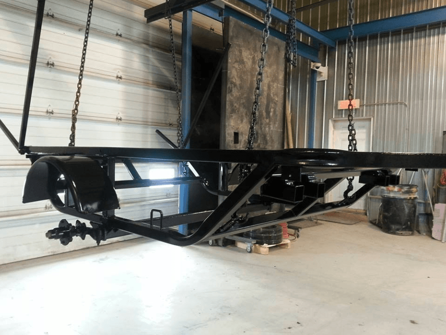 Une remorque noire est suspendue à des chaînes dans un garage.