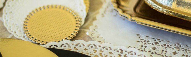 Un tappetino circolare dorato con decorazioni in rilievo è appoggiato su un centrino di carta bianca accanto a un vassoio dorato.