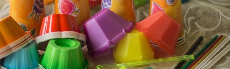 Su un tavolo sono sparsi un assortimento colorato di stampini di plastica per dessert impilati e bicchieri di carta decorati.