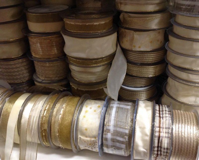 Uno scaffale pieno di rotoli di nastri decorativi di vario tipo, nei toni dell'oro, del crema, del beige e con motivi a quadri.