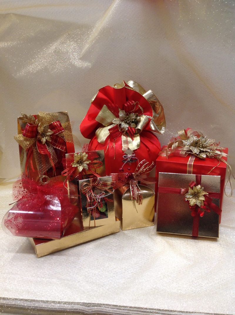 Scatole regalo assortite, avvolte in carta lucida rossa e dorata e decorate con fiocchi e nastri festivi.