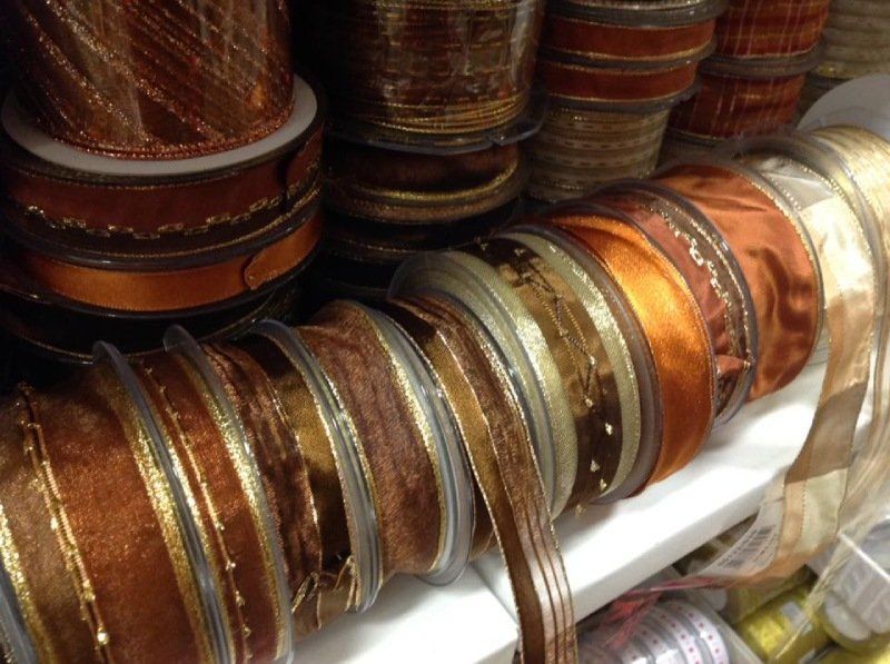 Rocchetti di nastro decorativo nelle tonalità del marrone, del bronzo e dell'oro impilati su uno scaffale bianco.