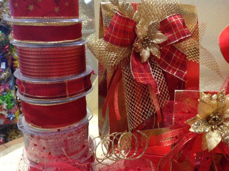 Una pila di nastri rossi e dorati accanto a un regalo avvolto in carta dorata metallizzata con un fiocco decorativo rosso e oro.