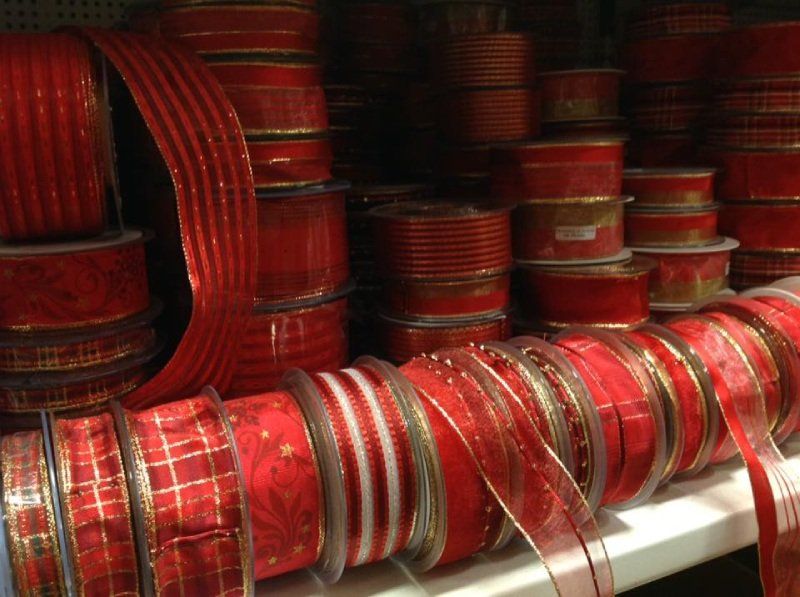 Scaffali pieni di rocchetti di nastro decorativo rosso di vario tipo, con diverse fantasie, trame e larghezze.