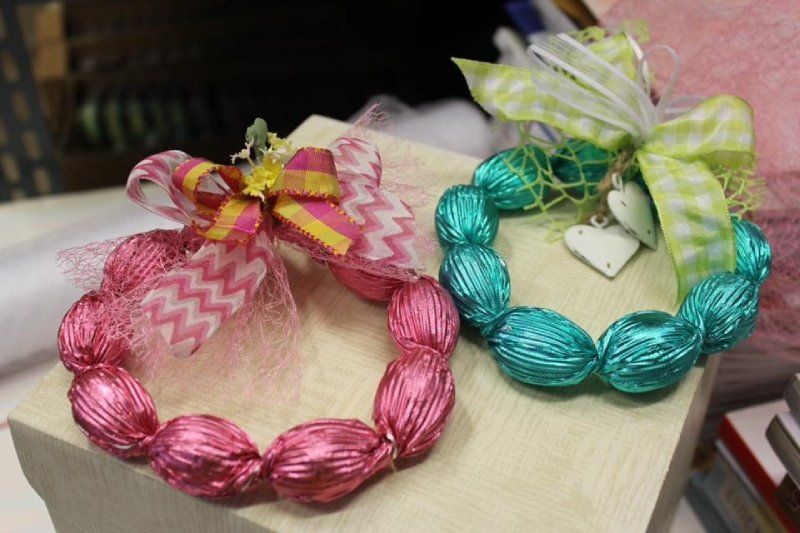 Due ghirlande composte da cioccolatini ovali avvolti in carta stagnola, una rosa e una verde acqua, esposte su una superficie di legno con fiocchi decorativi.