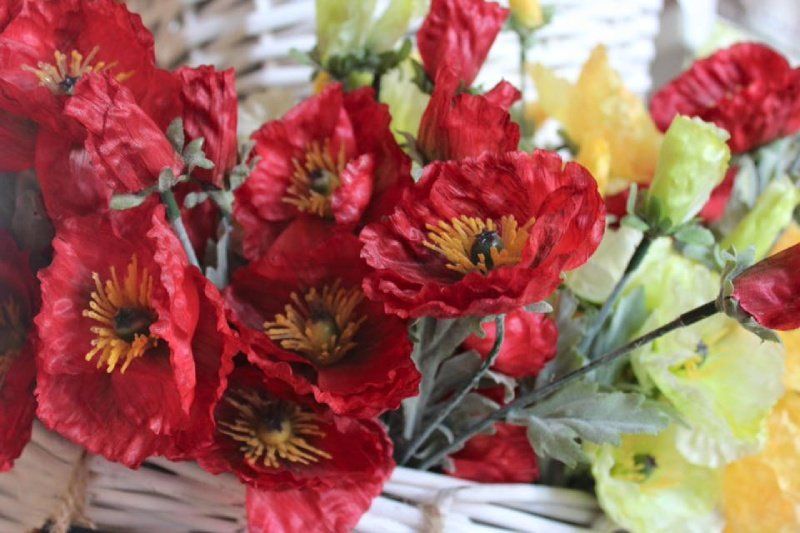 Un vivace bouquet di papaveri rossi artificiali e delicati fiori gialli adagiato in un cestino di vimini bianco.