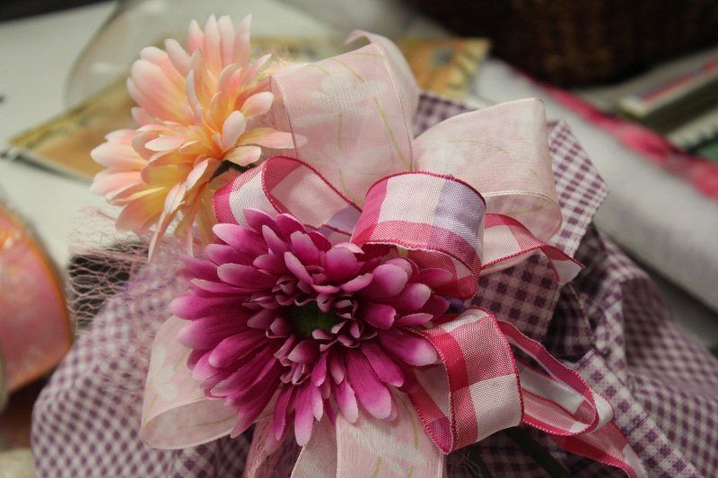 Una composizione floreale con un grande crisantemo rosa acceso e un fiore più piccolo color pesca, il tutto racchiuso in un fiocco a quadri.