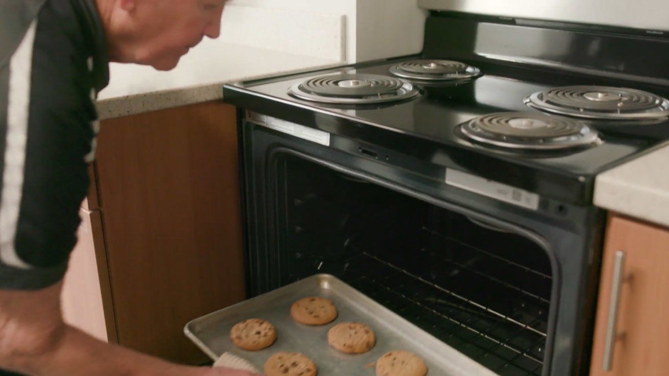 A man is taking a tray of cookies out of an oven.