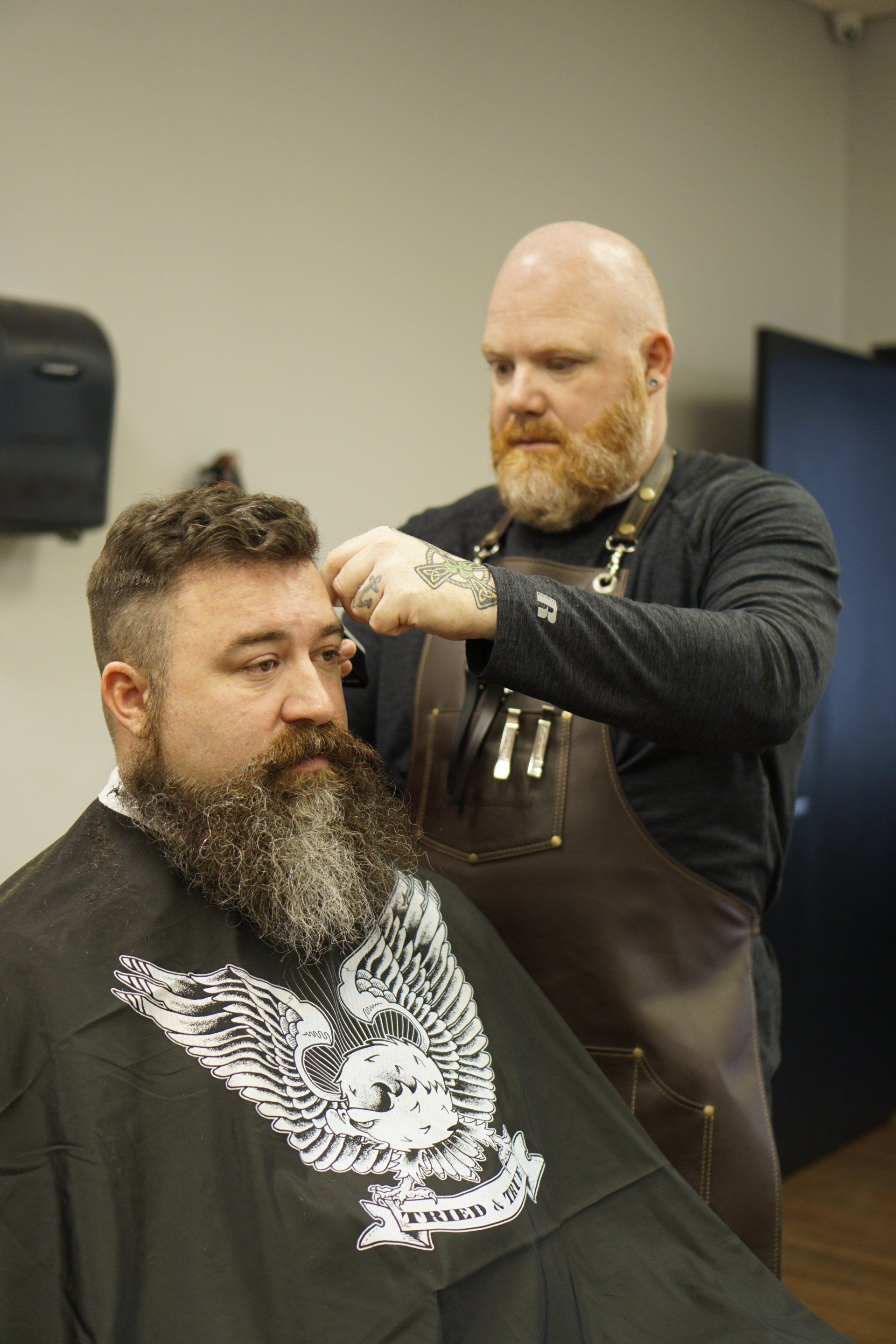 A man with a beard is getting his hair cut by a barber.