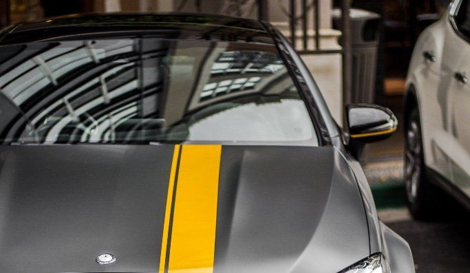 A gray car with yellow stripes on the hood is parked next to a white car.