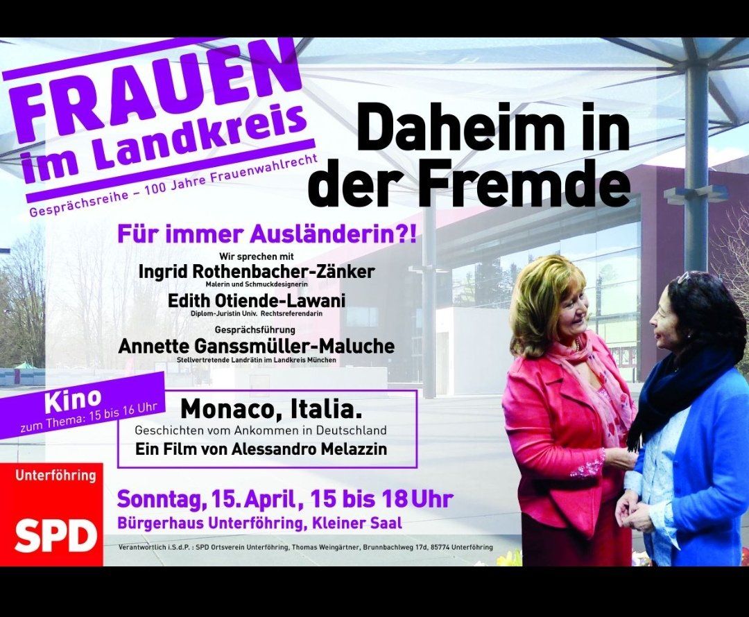 Two women are standing next to each other in front of a sign that says daheim in der fremde