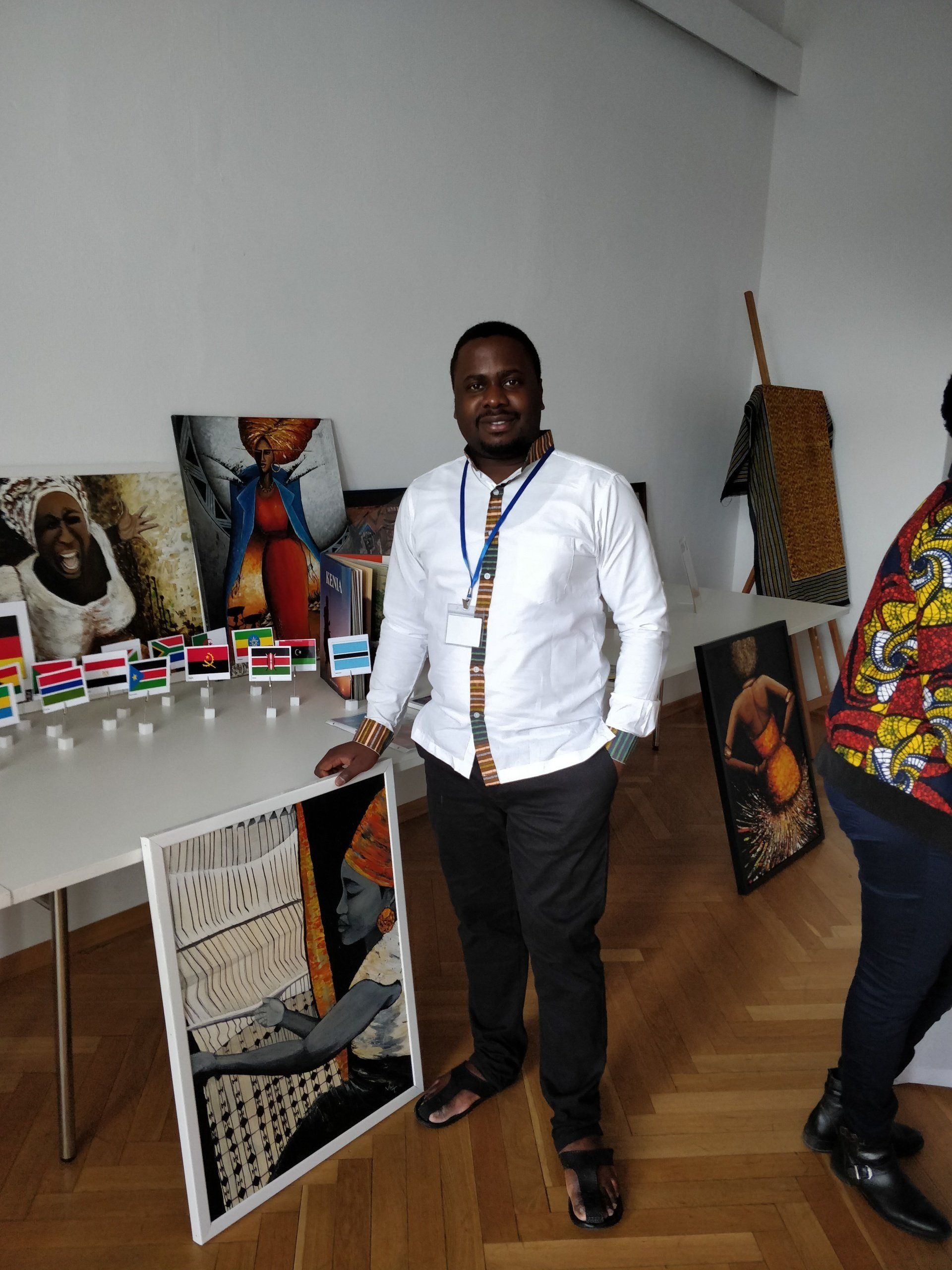 A man in a white shirt and tie is standing in front of a table with paintings on it.