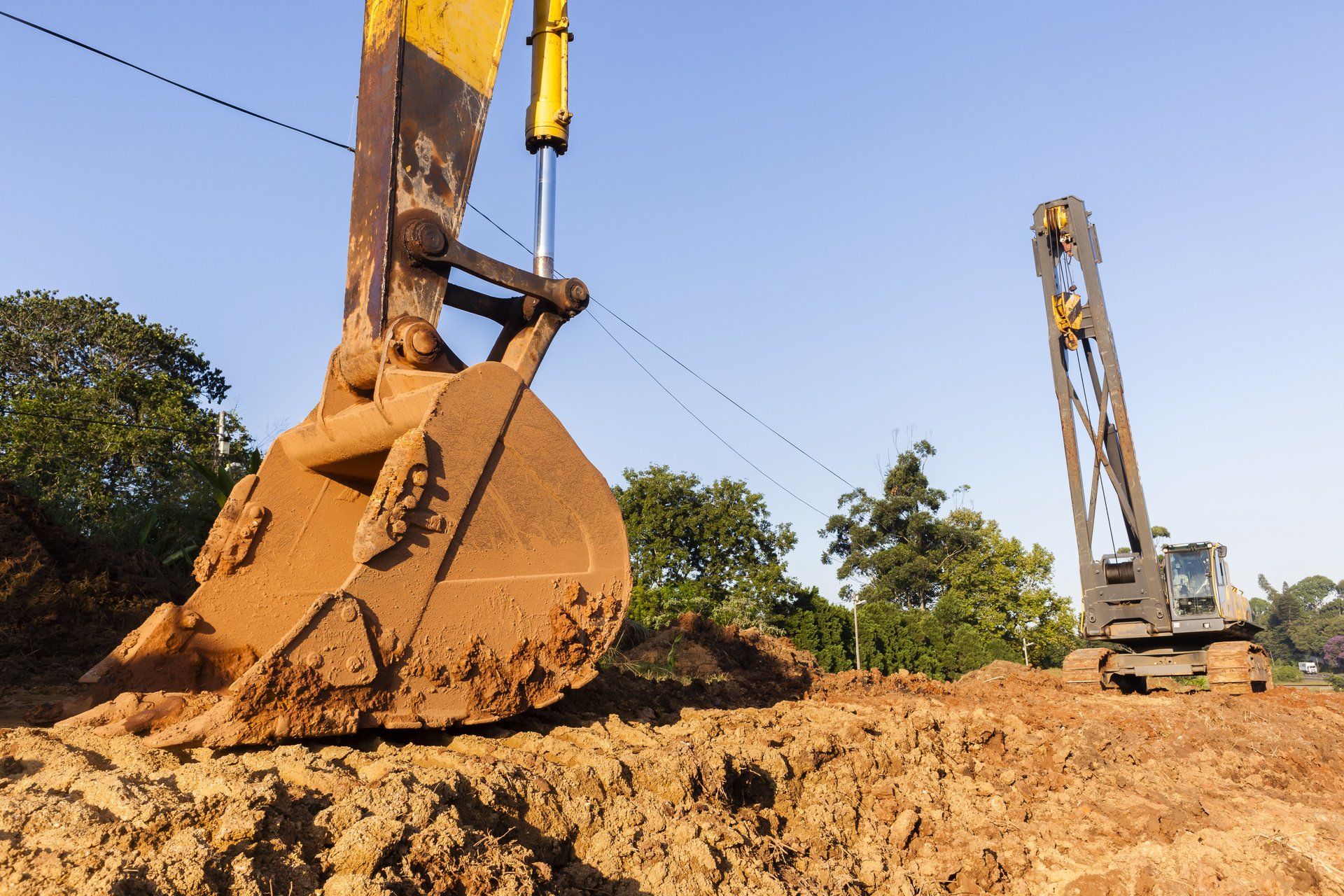 Ein gelber Bagger gräbt auf einer Baustelle ein Loch in die Erde.
