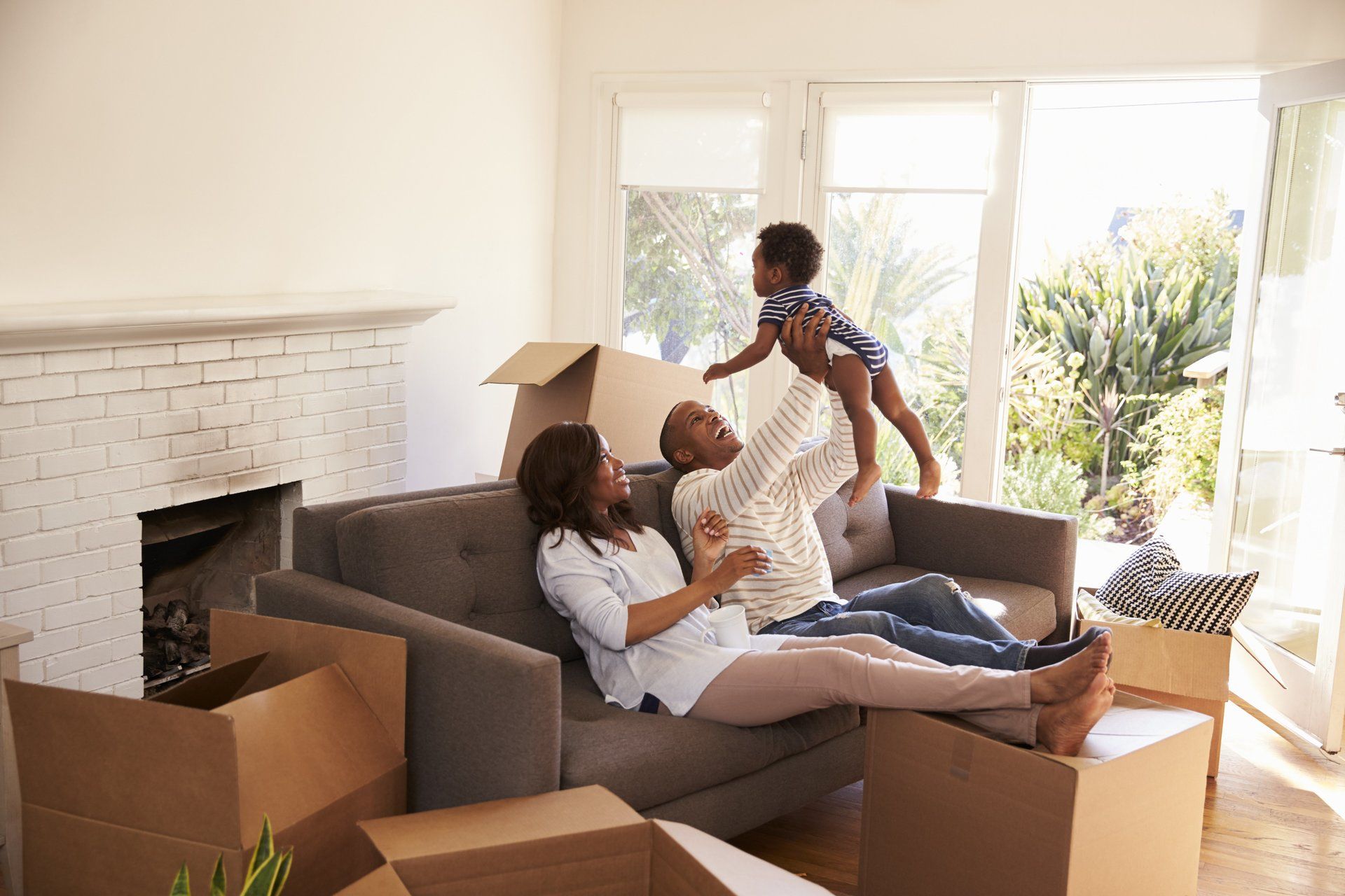 Eine Familie sitzt auf einer Couch in einem Wohnzimmer, umgeben von Pappkartons.