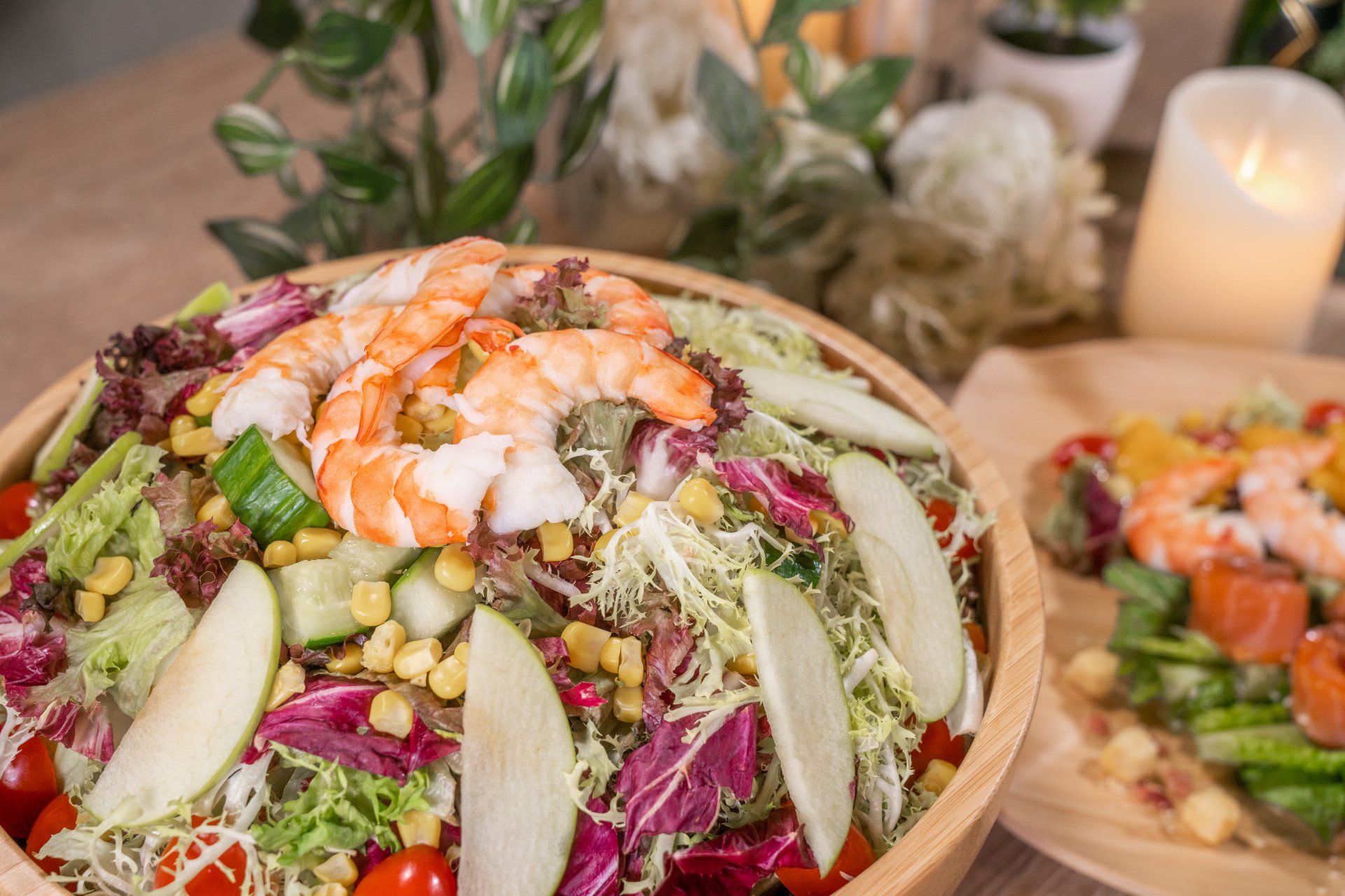 Shrimp salad in a wooden bowl with mixed greens, apple slices, and corn.