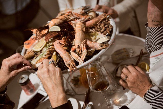 Mensen hadden zich verzameld rond een grote schaal met zeevruchten, waaronder garnalen, aan een restauranttafel.