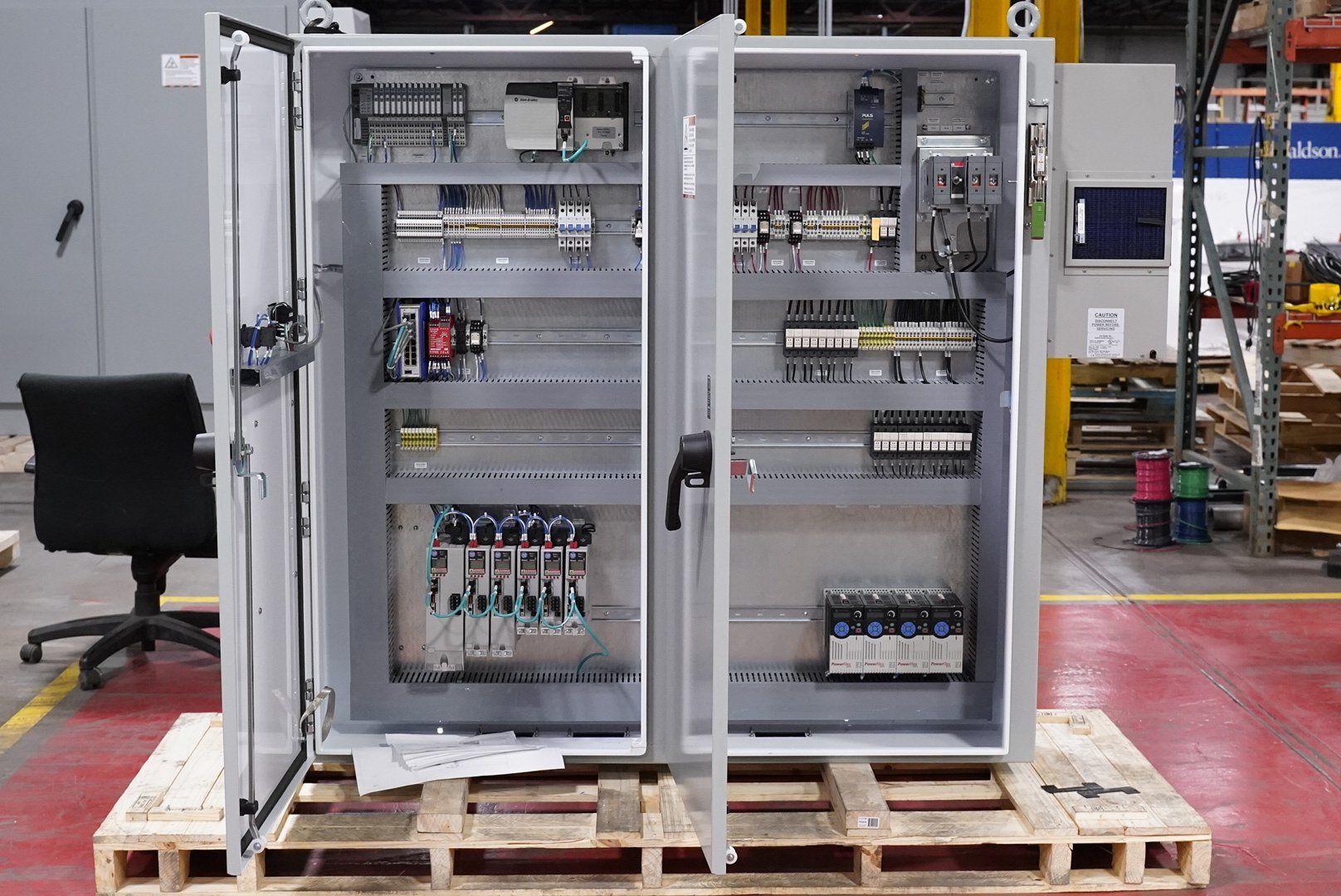 Opened electrical control panel on a pallet, with various components and wiring visible.