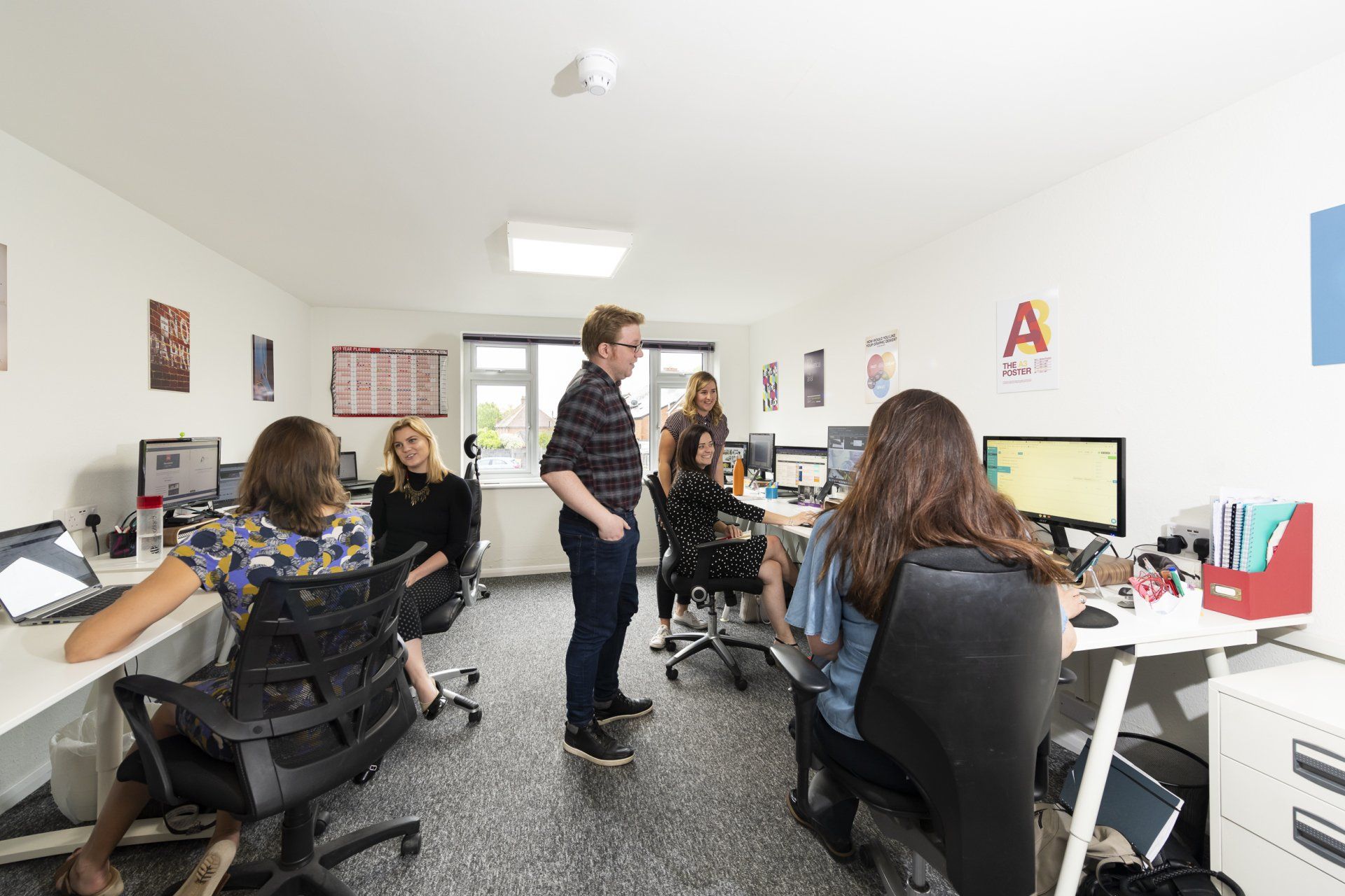 A group of people are standing in an office talking to each other.